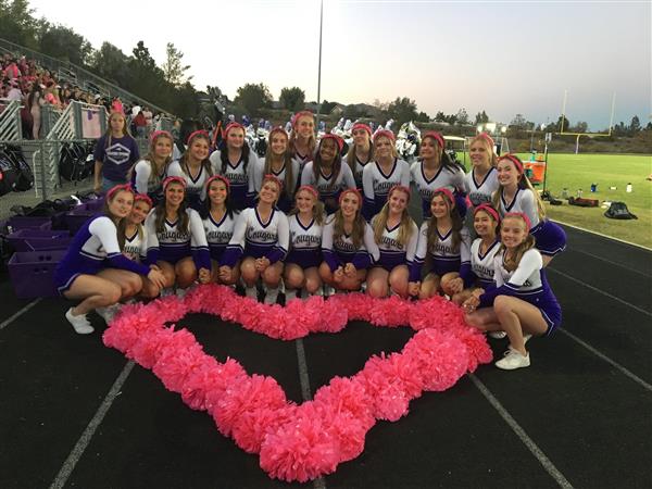 Spanish Springs Cougars cheer team on the track at Spanish Springs posed around a pink heart made out of cheer pom poms.